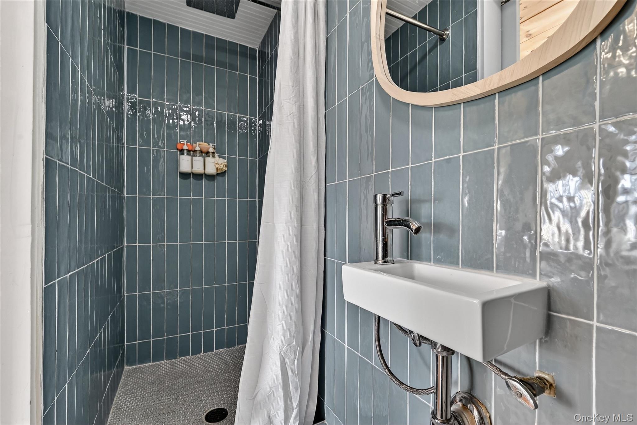 96 Lower Wisner Road Warwick, NY 10990 - Photo 26 of 34 Bathroom featuring a wall-mounted rectangular basin sink with chrome faucet, a wooden framed mirror, and vertical blue subway tile shower surround with a white shower curtain