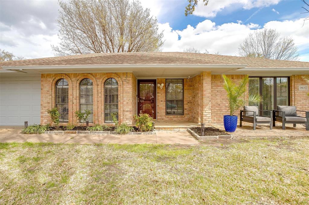 View of front of house with a front yard, covered porch, an attached garage, brick siding, and a shingled roof
