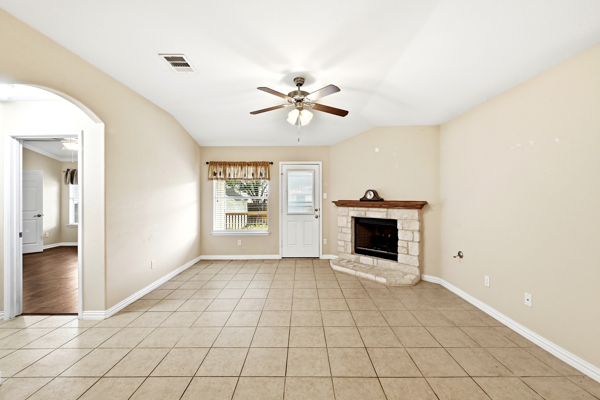 209 Calline Mayes Run Buda, TX 78610 - Photo 17 of 32 Living area featuring neutral-toned tile flooring, a corner fireplace with stone surround and wood mantel, and a ceiling fan with integrated lighting