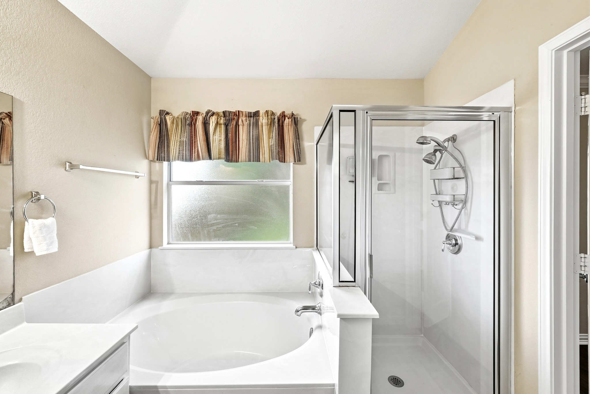 209 Calline Mayes Run Buda, TX 78610 - Photo 23 of 32 Bathroom featuring a built-in soaking tub, a separate glass-enclosed shower with multiple showerheads, a vanity with a white countertop, and a window for natural light