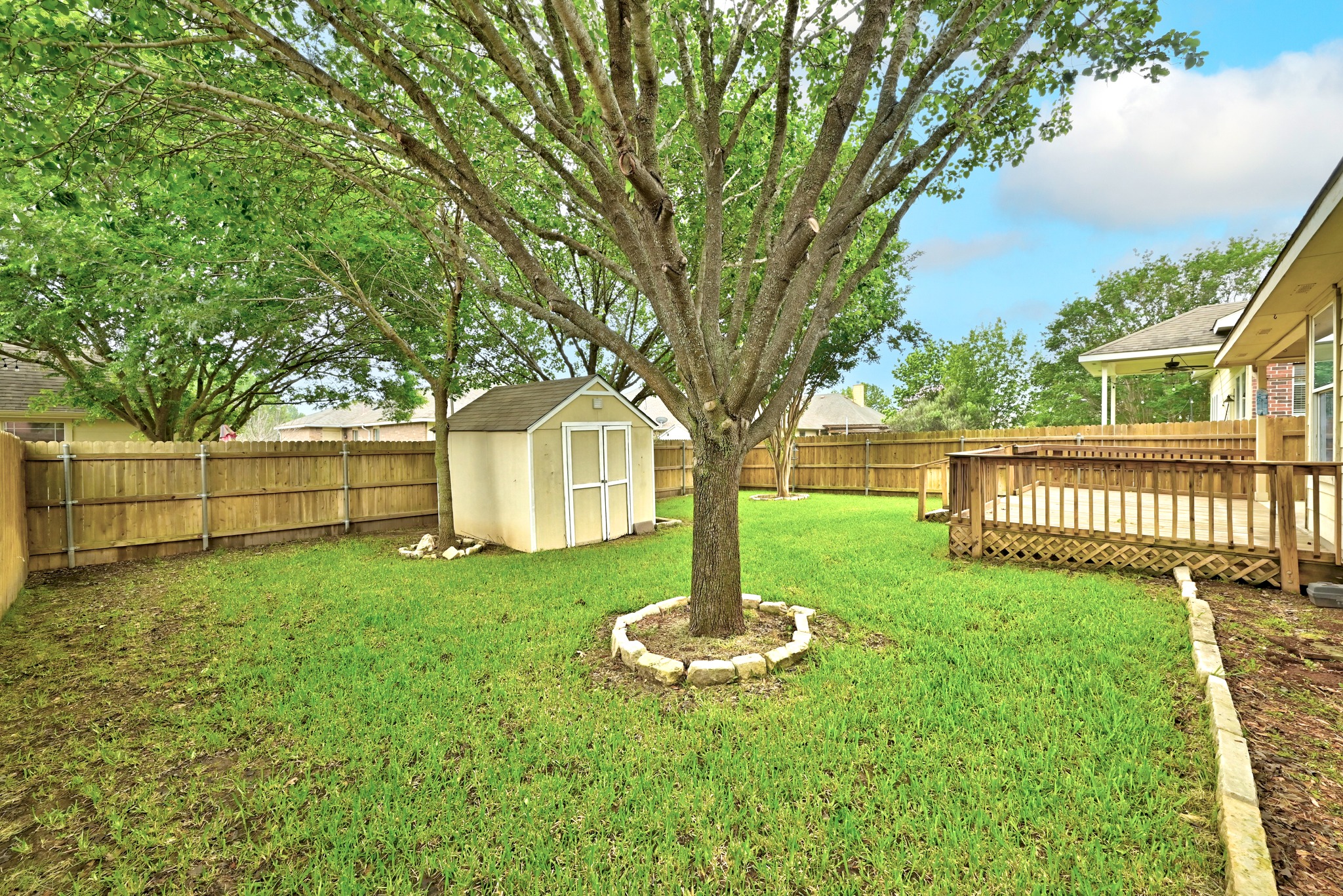 209 Calline Mayes Run Buda, TX 78610 - Photo 29 of 32 Expansive fenced backyard featuring a large established tree, a wooden storage shed, and a multi-level wooden deck