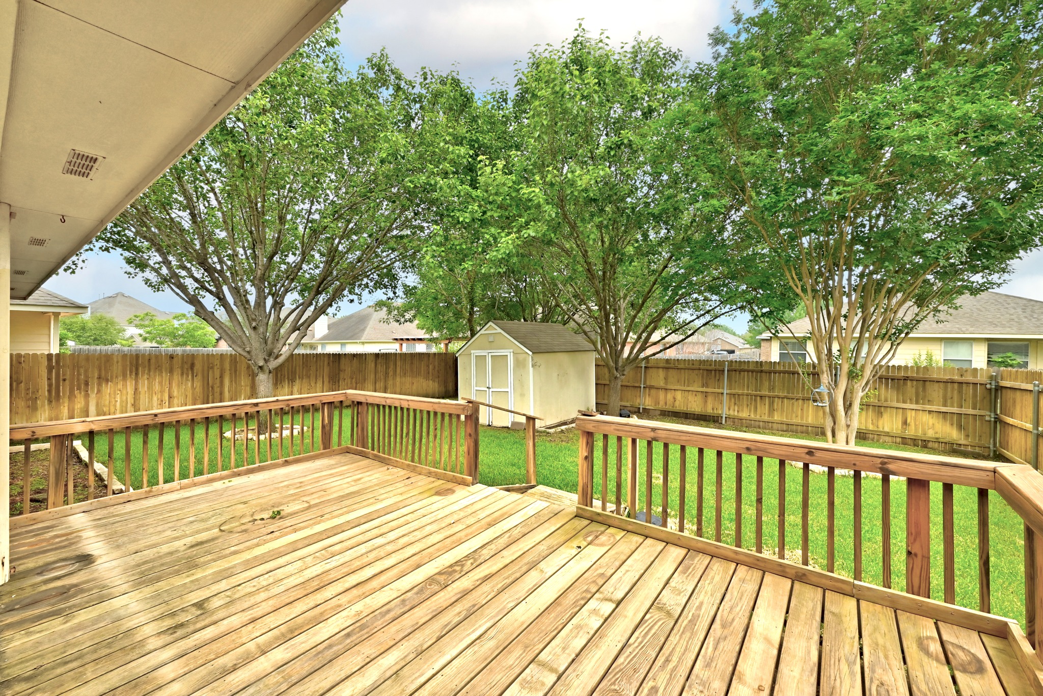 209 Calline Mayes Run Buda, TX 78610 - Photo 31 of 32 Spacious wood-finish deck with railing, overlooking a fenced backyard with mature trees and a storage shed