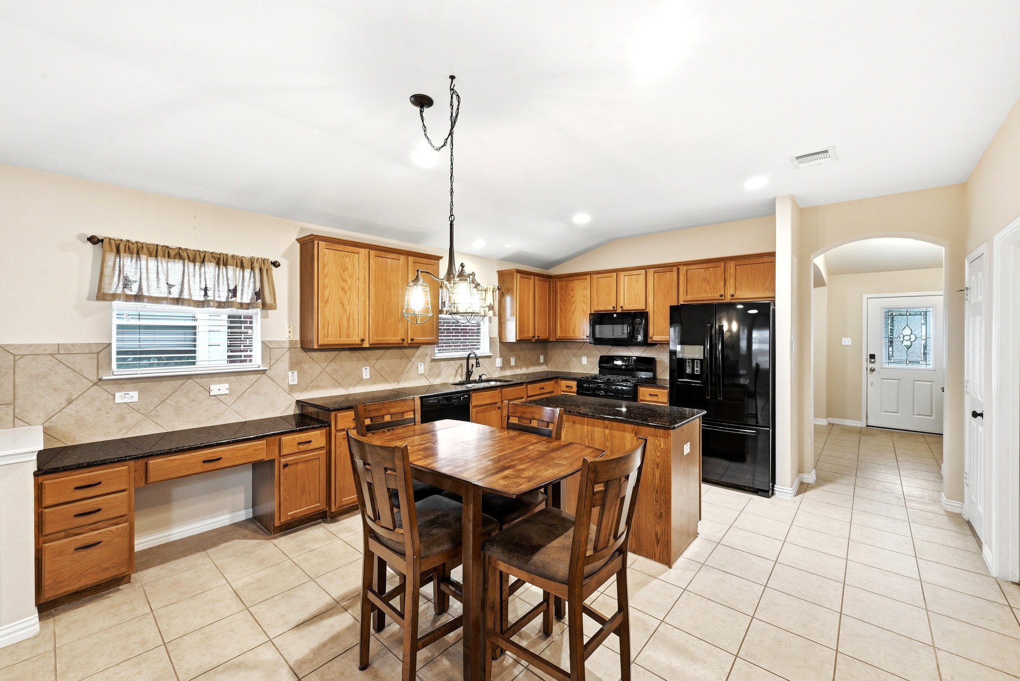 209 Calline Mayes Run Buda, TX 78610 - Photo 10 of 32 Open-concept kitchen with light wood cabinetry, dark countertops, black appliances, and neutral tile flooring
