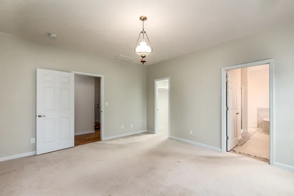 an empty room that has a chandelier fan and kitchen view