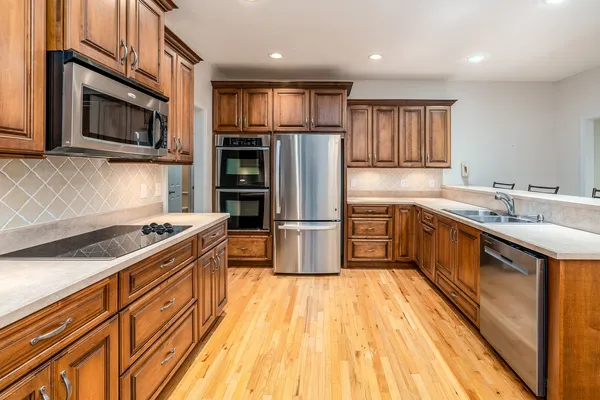 a kitchen with stainless steel appliances granite countertop a stove top oven a sink dishwasher a refrigerator and a microwave oven with wooden floor