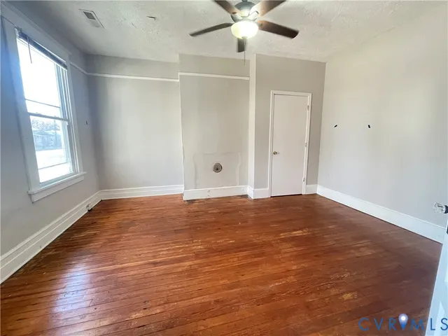 an empty room with wooden floor fan and windows