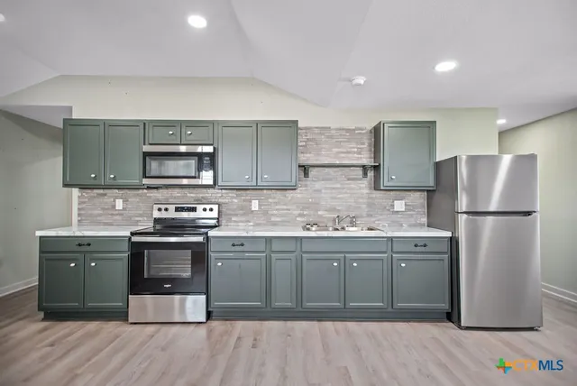 a kitchen with stainless steel appliances granite countertop a stove top oven a sink and a refrigerator