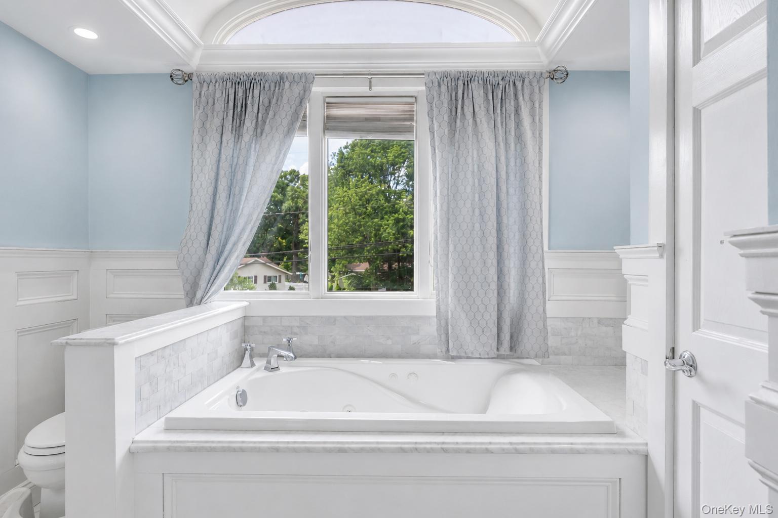 19 Joan Road Bay Shore, NY 11706 - Photo 29 of 50 Deep soaking tub with polished chrome fixtures, surrounded by white wainscoting and light marble-finish tile