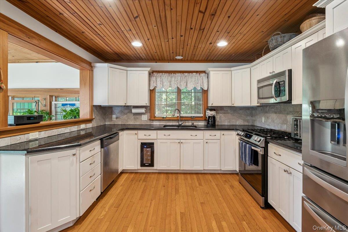 342 Lake Shore Road Putnam Valley, NY 10579 - Photo 12 of 46 Kitchen with appliances with stainless steel finishes, wood ceiling, white cabinetry, light wood-style flooring, and backsplash