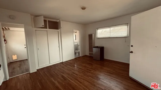a view of an empty room with wooden floor and a bathroom