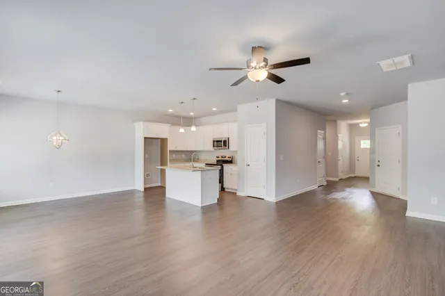 a view of an empty room and kitchen with wooden floor