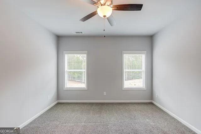 an empty room with chandelier fan and windows