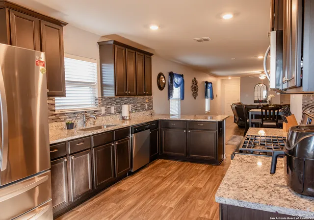 a kitchen with stainless steel appliances granite countertop a refrigerator a sink dishwasher a stove with wooden cabinets and floor