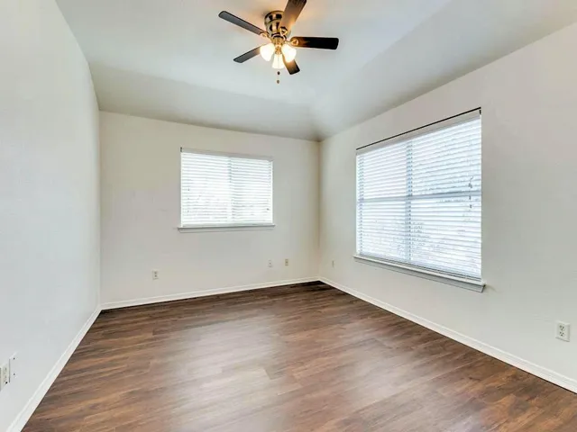 an empty room with wooden floor ceiling fan and windows