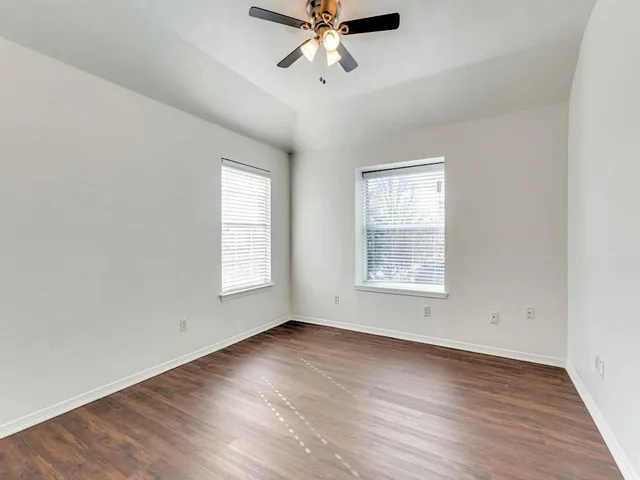 an empty room with wooden floor chandelier fan and windows