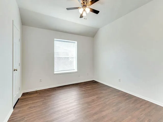 an empty room with wooden floor chandelier fan and windows