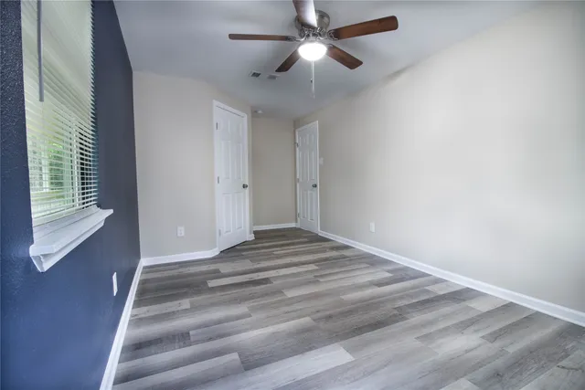 a view of empty room with wooden floor and fan