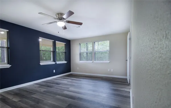 an empty room with wooden floor fan and windows
