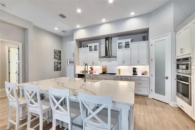 a kitchen with stainless steel appliances kitchen island granite countertop a stove a sink a refrigerator white cabinets and wooden floor