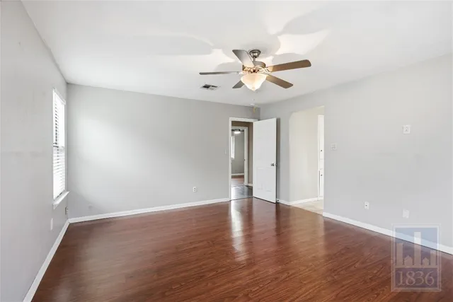 a view of an empty room with wooden floor and a ceiling fan