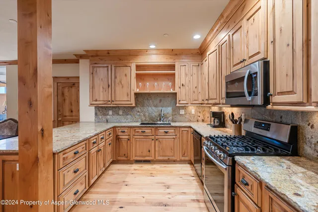 a open kitchen with stainless steel appliances granite countertop a stove top oven a sink dishwasher and a microwave oven with large trees