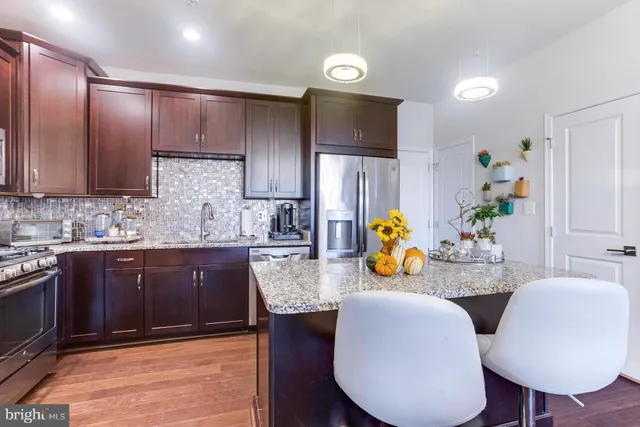 a kitchen with stainless steel appliances kitchen island granite countertop a table chairs in it and wooden floors