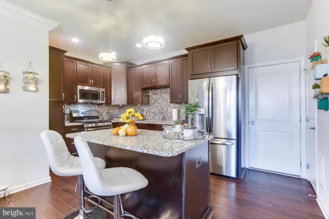 a kitchen with stainless steel appliances granite countertop a refrigerator a stove a sink dishwasher a dining table and chairs with wooden floor