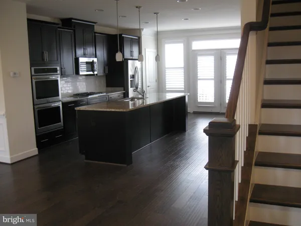 a kitchen with stainless steel appliances wooden floors wooden cabinets a refrigerator and a sink