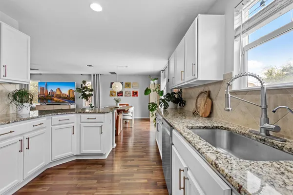 a kitchen with stainless steel appliances granite countertop a sink dishwasher stove and white cabinets with wooden floor