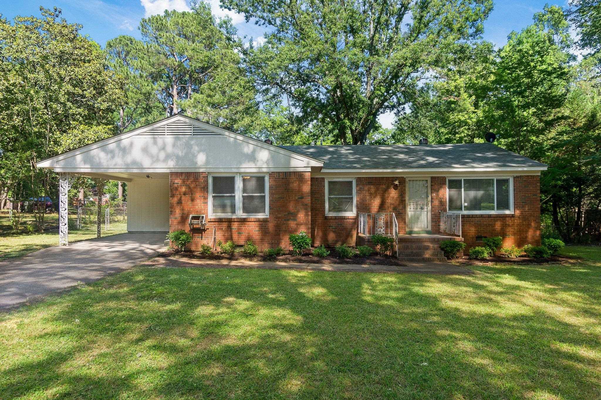 Ranch-style house featuring a front lawn, driveway, brick siding, and a carport