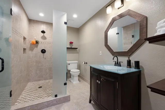a spacious bathroom with a granite countertop sink a toilet a mirror and shower