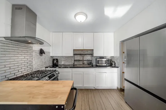 a kitchen with stainless steel appliances granite countertop a stove top oven a sink a refrigerator white cabinets and wooden floor