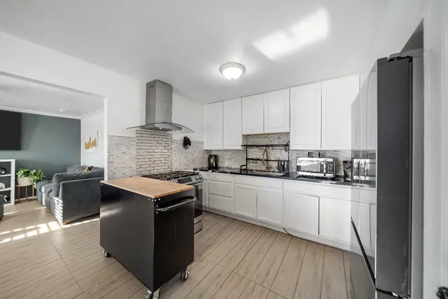 a kitchen with stainless steel appliances kitchen island granite countertop a stove a refrigerator a dining table and chairs with wooden floor