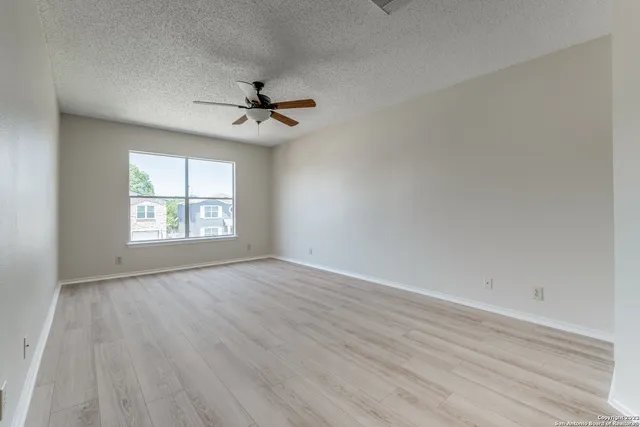 an empty room with wooden floor ceiling fan and windows
