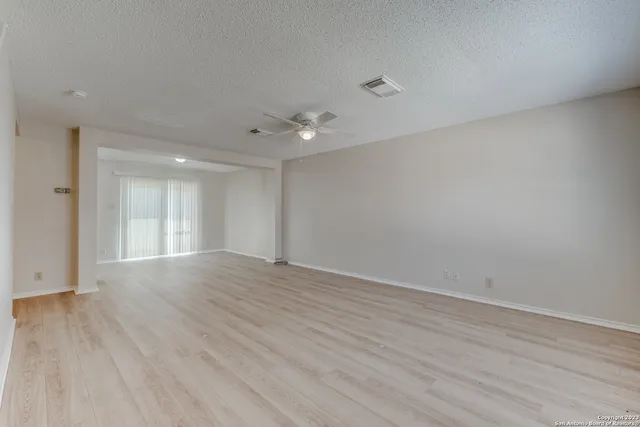 a view of an empty room with wooden floor and a ceiling fan