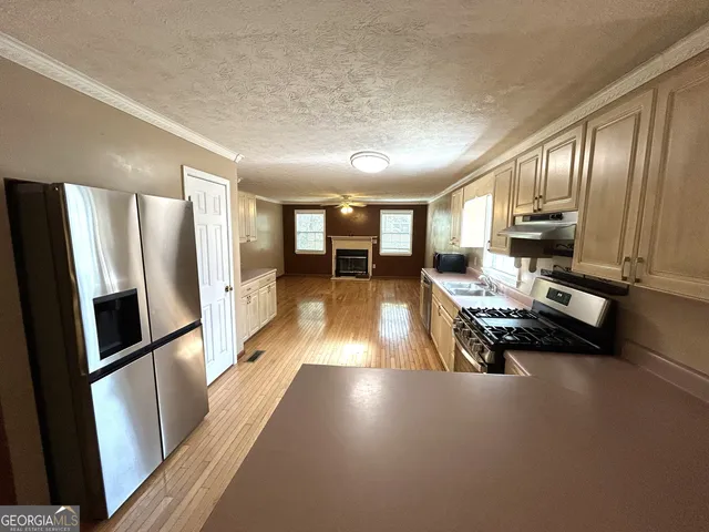 a kitchen with stainless steel appliances granite countertop a refrigerator a sink dishwasher a stove and white countertops with wooden floor