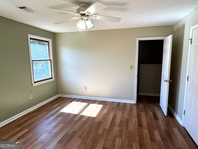 an empty room with wooden floor windows and fan