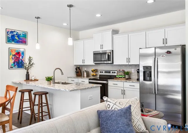 a kitchen with stainless steel appliances kitchen island granite countertop a refrigerator a sink a stove and white cabinets