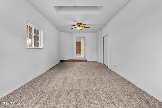 an empty room with chandelier fan and windows