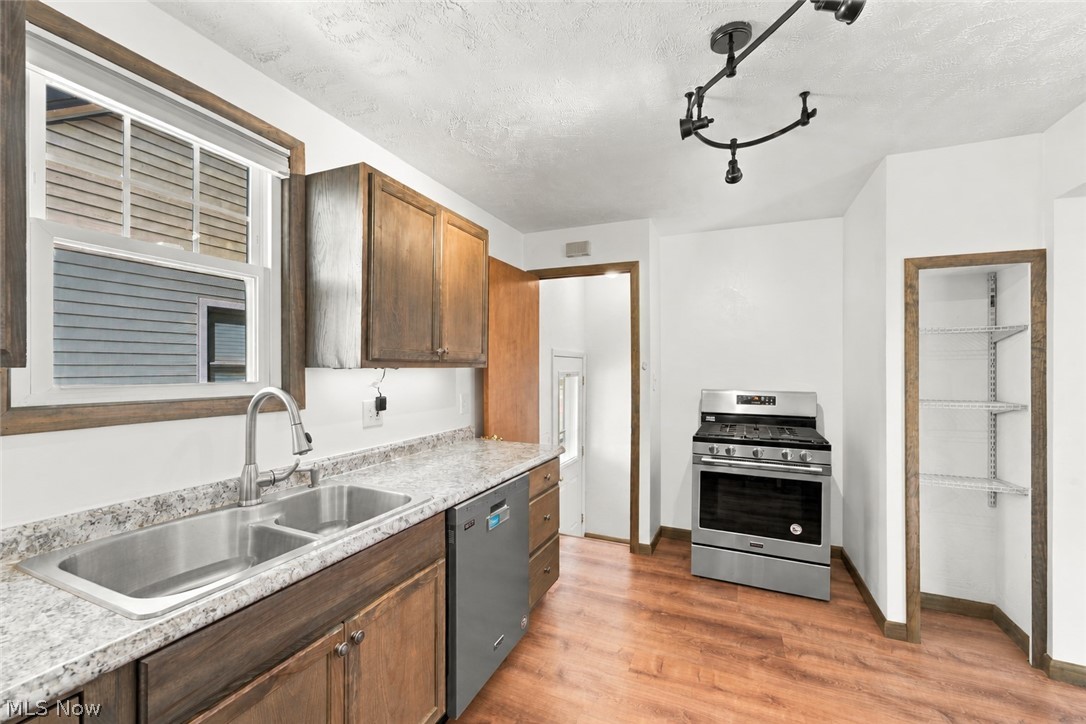 1434 Sunset Road Mayfield Heights, OH 44124 - Photo 22 of 36 Wood-finish flooring, stainless steel gas range, dual basin stainless steel sink, wood cabinetry, and track lighting