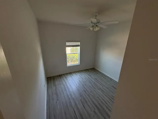 an empty room with wooden floor fan and windows