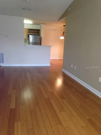 a view of empty room with wooden floor and kitchen