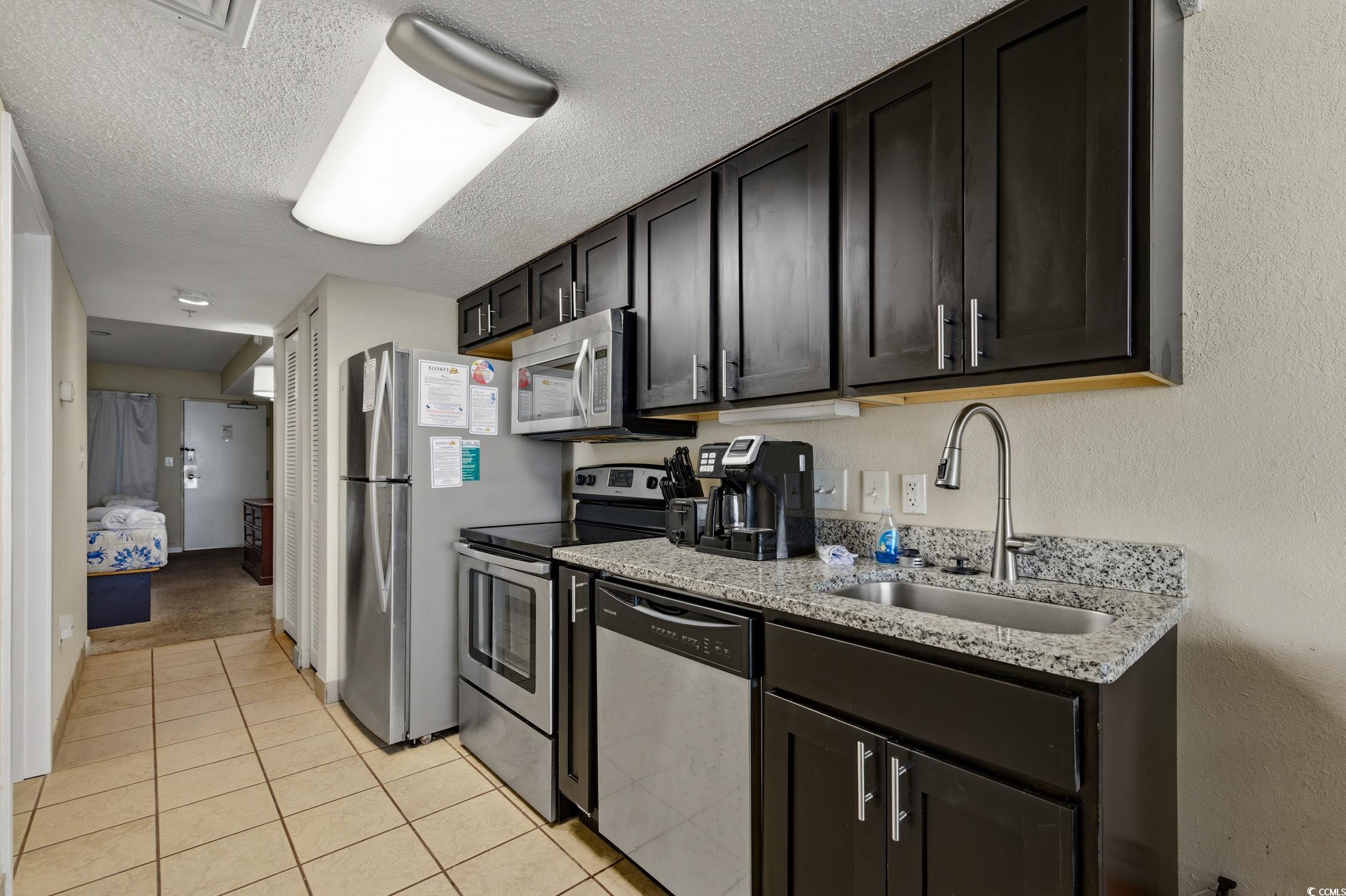 1702 North Ocean Boulevard, Unit 355 Myrtle Beach, SC 29577 - Photo 6 of 27 Kitchen with appliances with stainless steel finishes, a textured ceiling, light stone countertops, and light tile patterned floors
