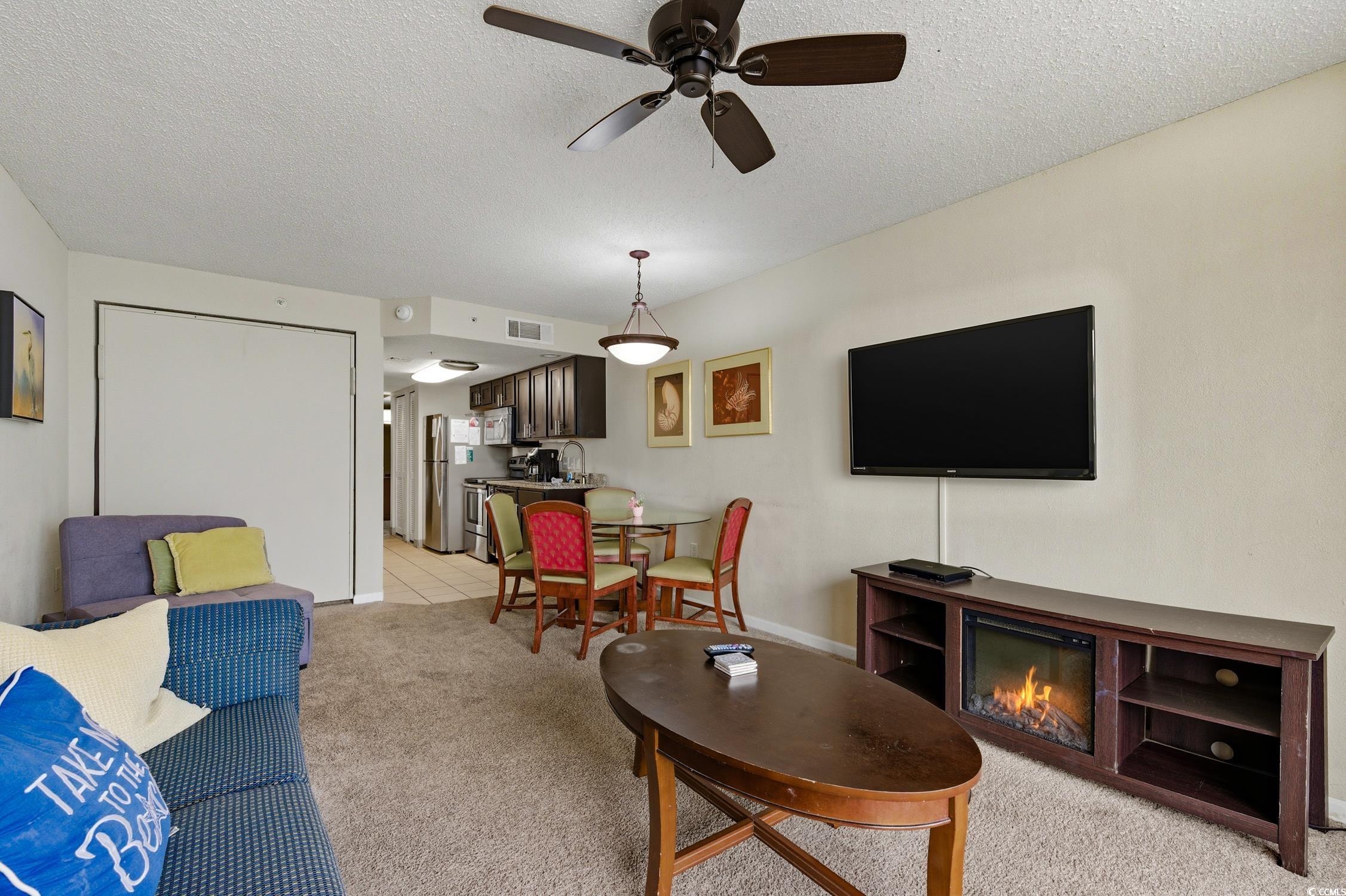 1702 North Ocean Boulevard, Unit 355 Myrtle Beach, SC 29577 - Photo 10 of 27 Living room with a textured ceiling, ceiling fan, light carpet, and a glass covered fireplace
