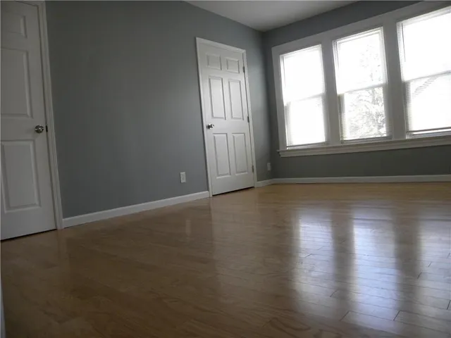 an empty room with wooden floor and windows with curtains