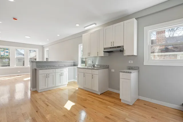 a kitchen with granite countertop a stove a sink and white cabinets with wooden floor