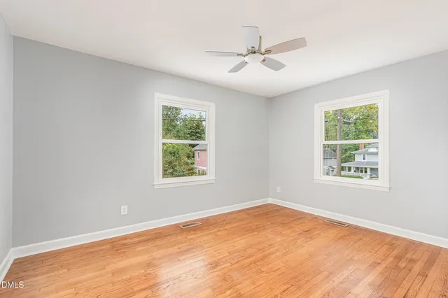 an empty room with wooden floor fan and windows