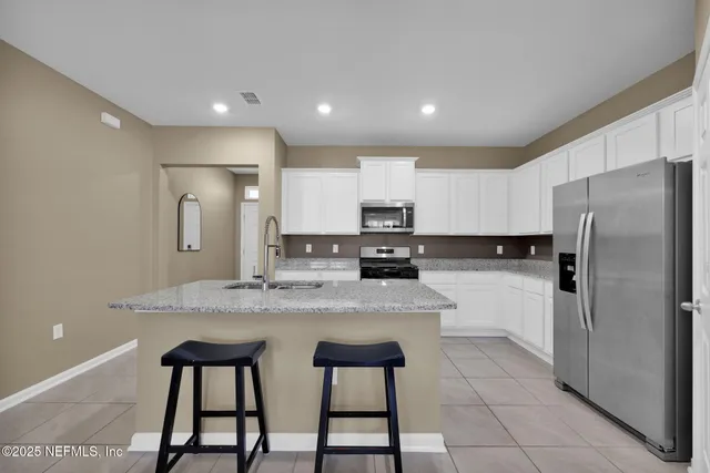 a kitchen with stainless steel appliances granite countertop a refrigerator a stove a sink and white cabinets with wooden floor