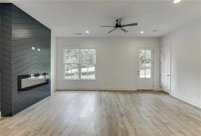 an empty room with wooden floor a ceiling fan and windows