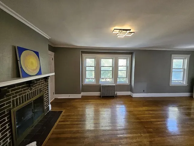 a view of an empty room with wooden floor a fireplace and a window